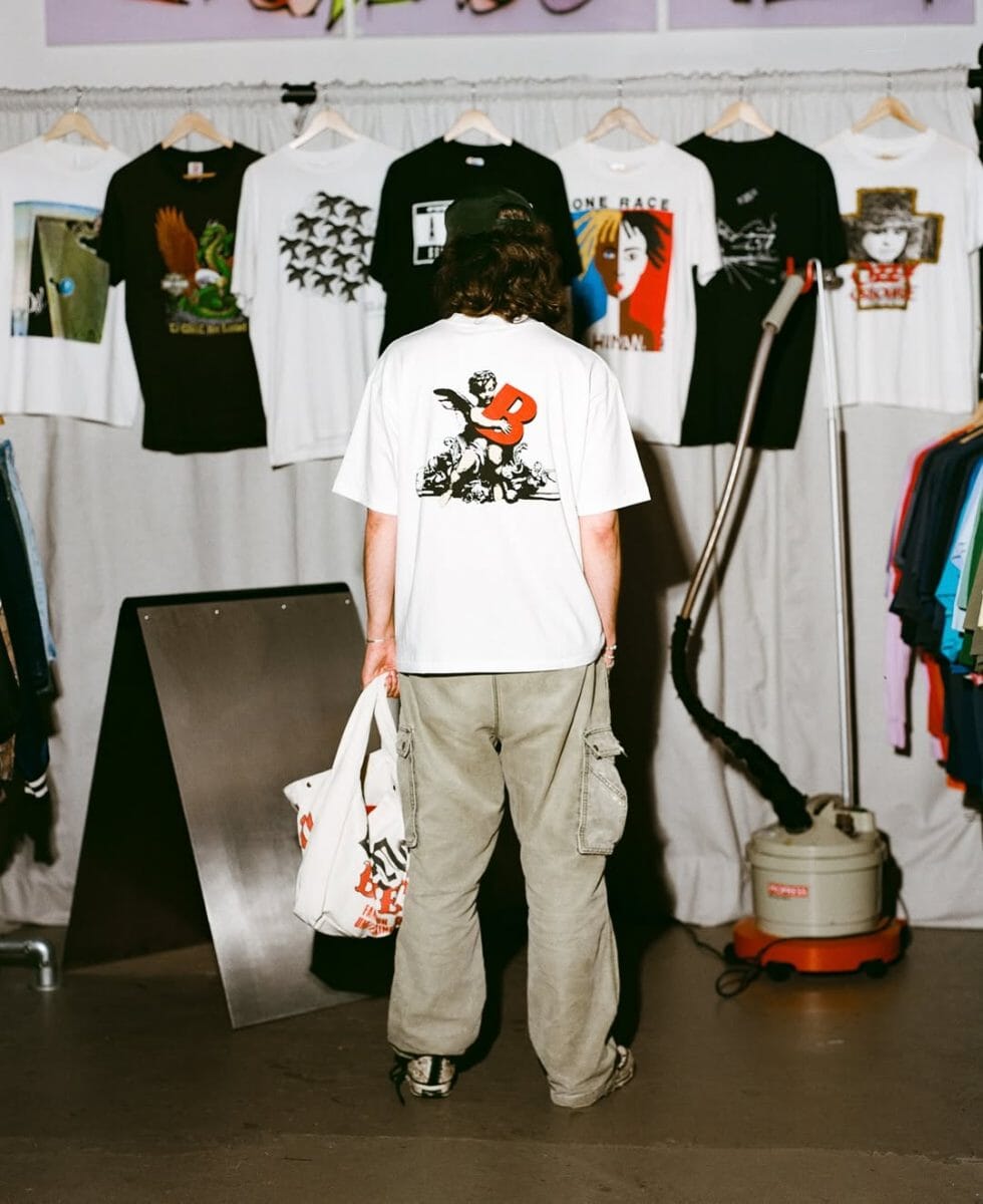 Person browsing graphic tees and holding a branded tote bag.