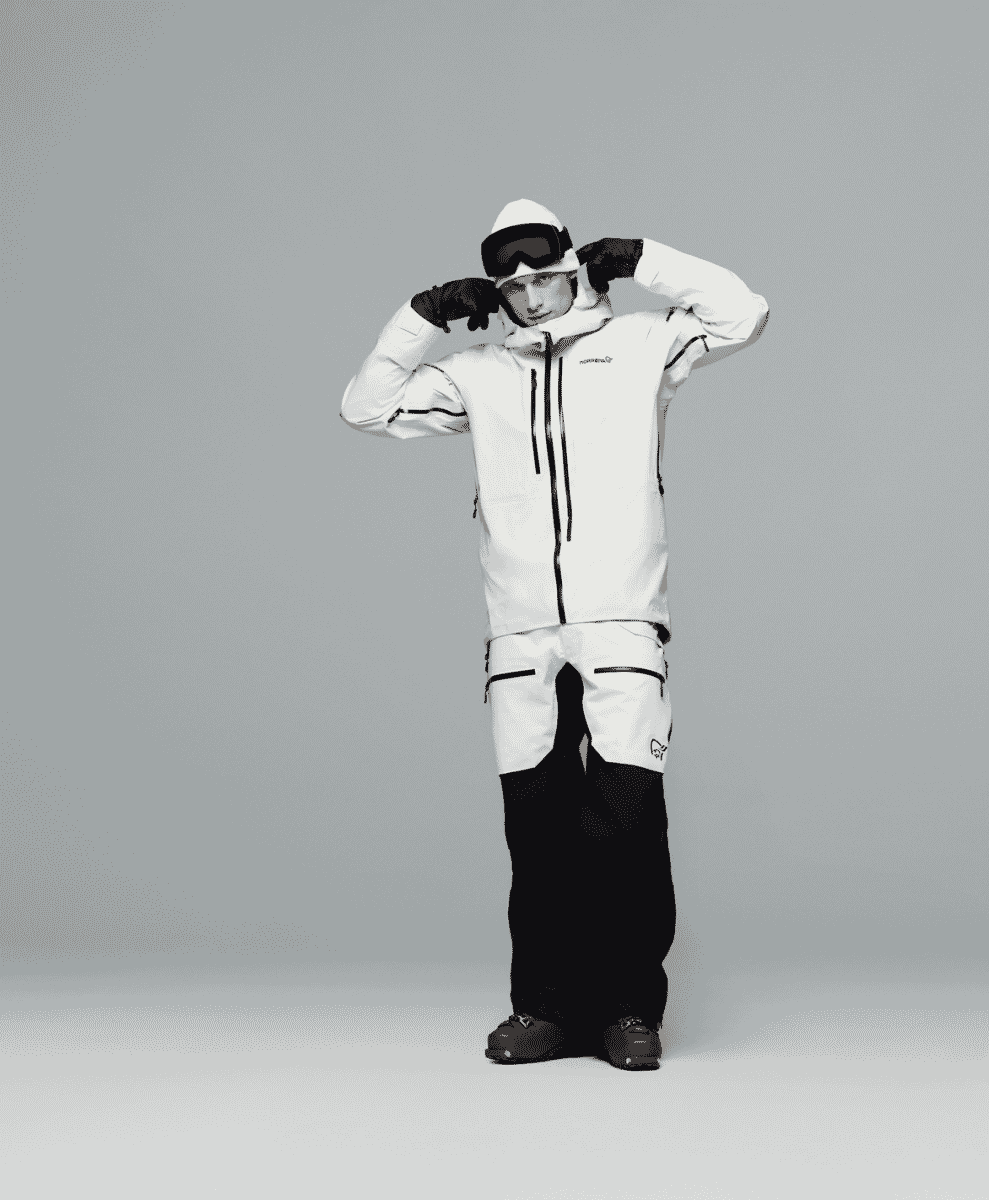 A model in a white Norrøna ski jacket and pants against a neutral gray background.