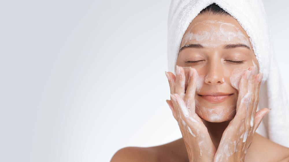 Close-up shot of a woman gently applying white foaming cleanser to her face.