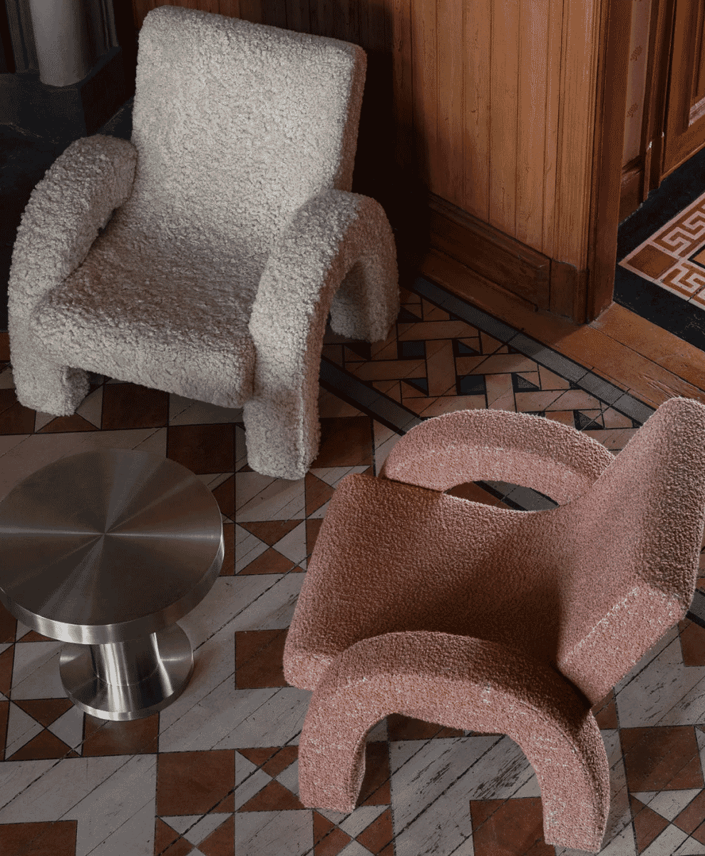 Two modern bouclé armchairs in cream and dusty pink colors on a geometric tiled floor.