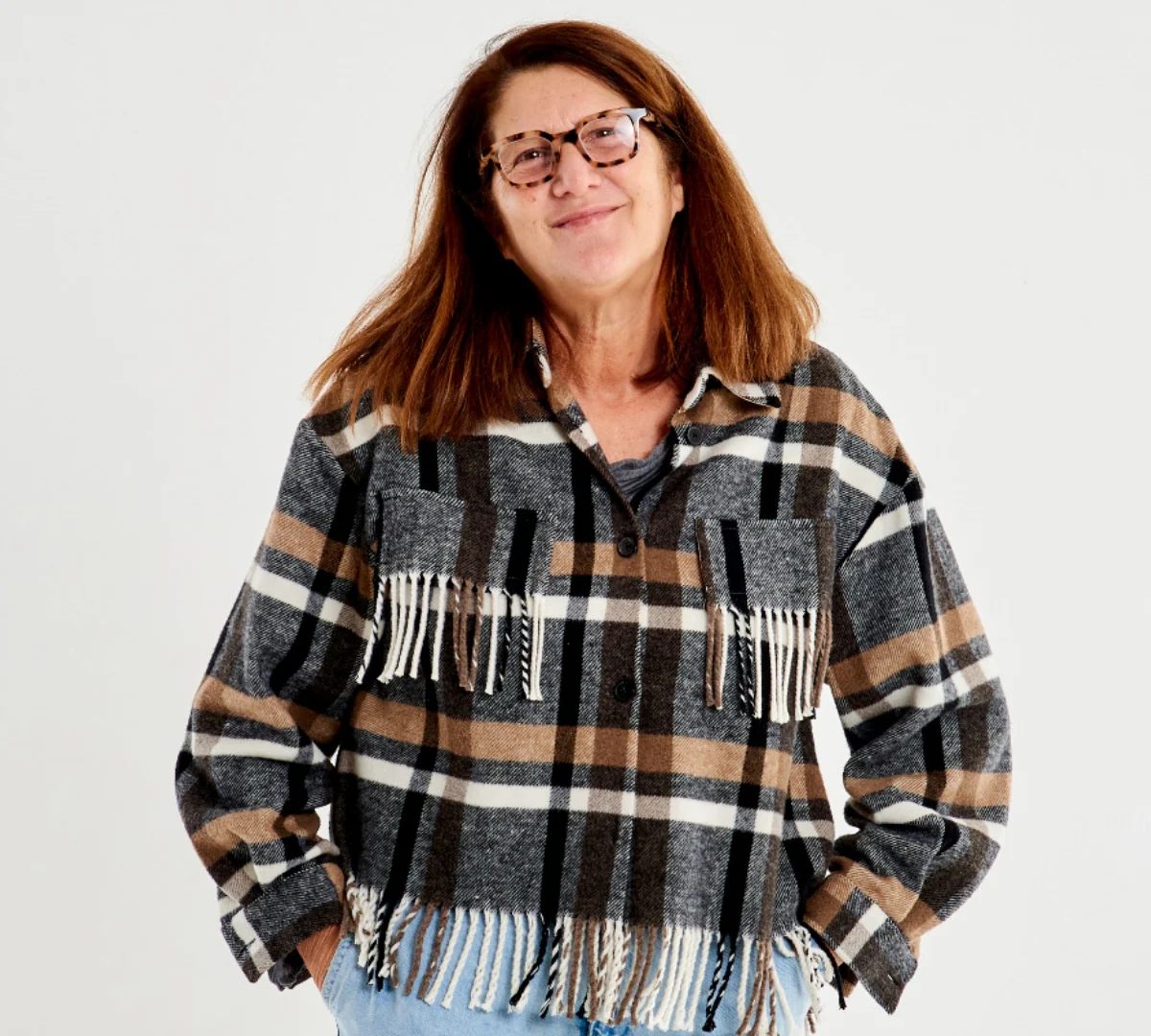 A woman wearing a plaid fringed jacket in earth tones over blue jeans and a gray shirt.