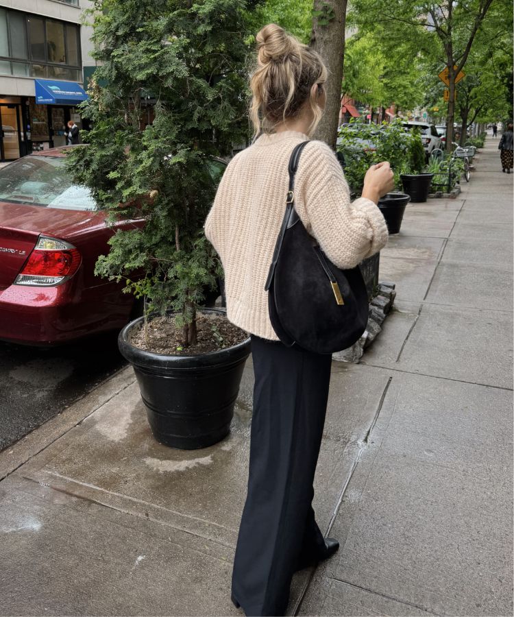A full-body shot of a model wearing relaxed pleated trousers and a soft knit sweater.