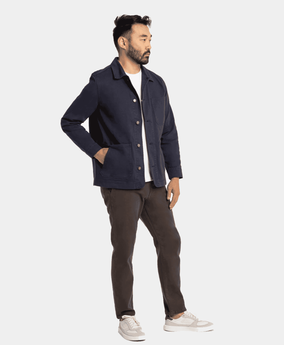 A man wearing a navy button-up work jacket over a white t-shirt and brown pants.