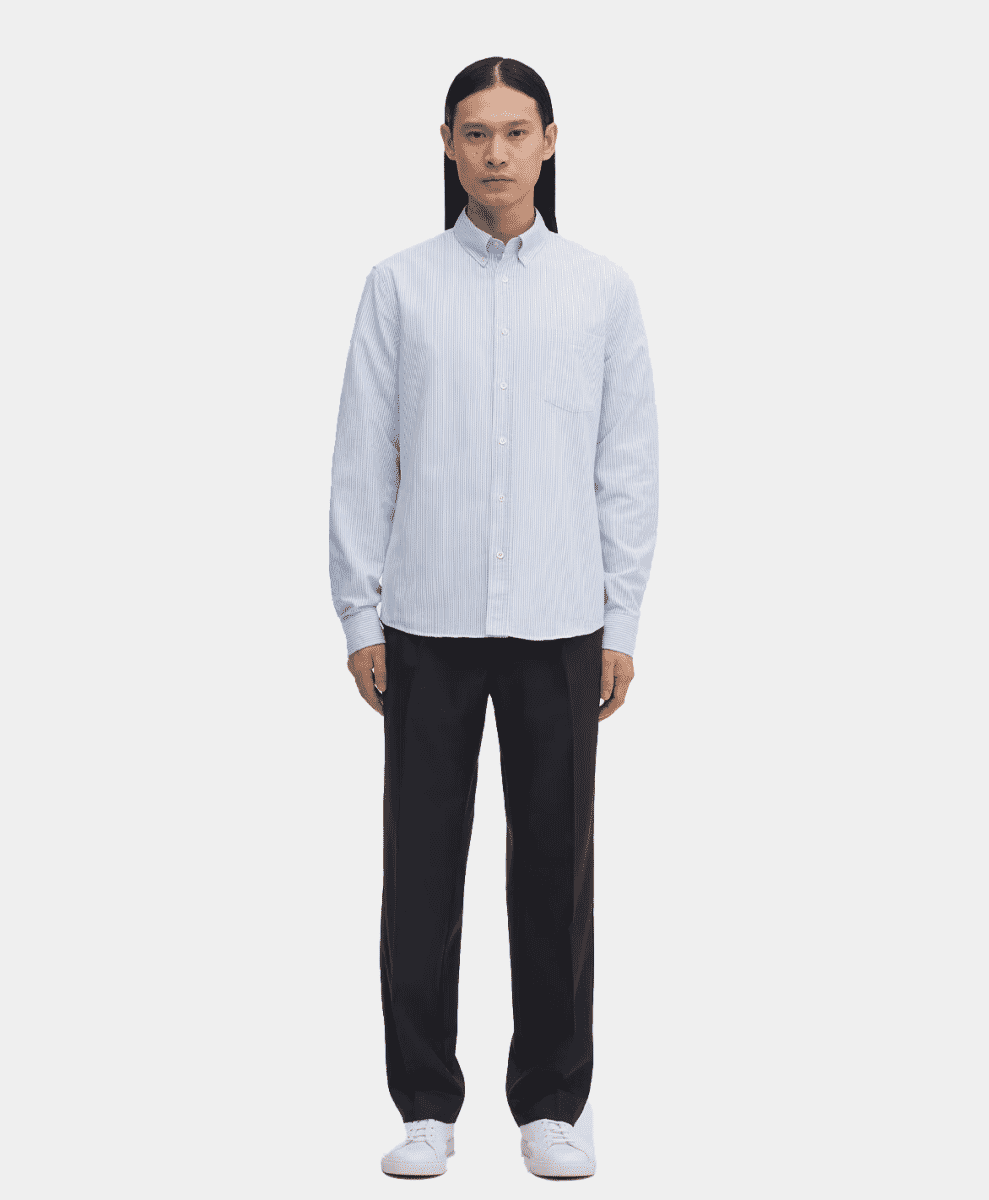 A man wearing a light blue and white vertically striped button-up shirt with black trousers.