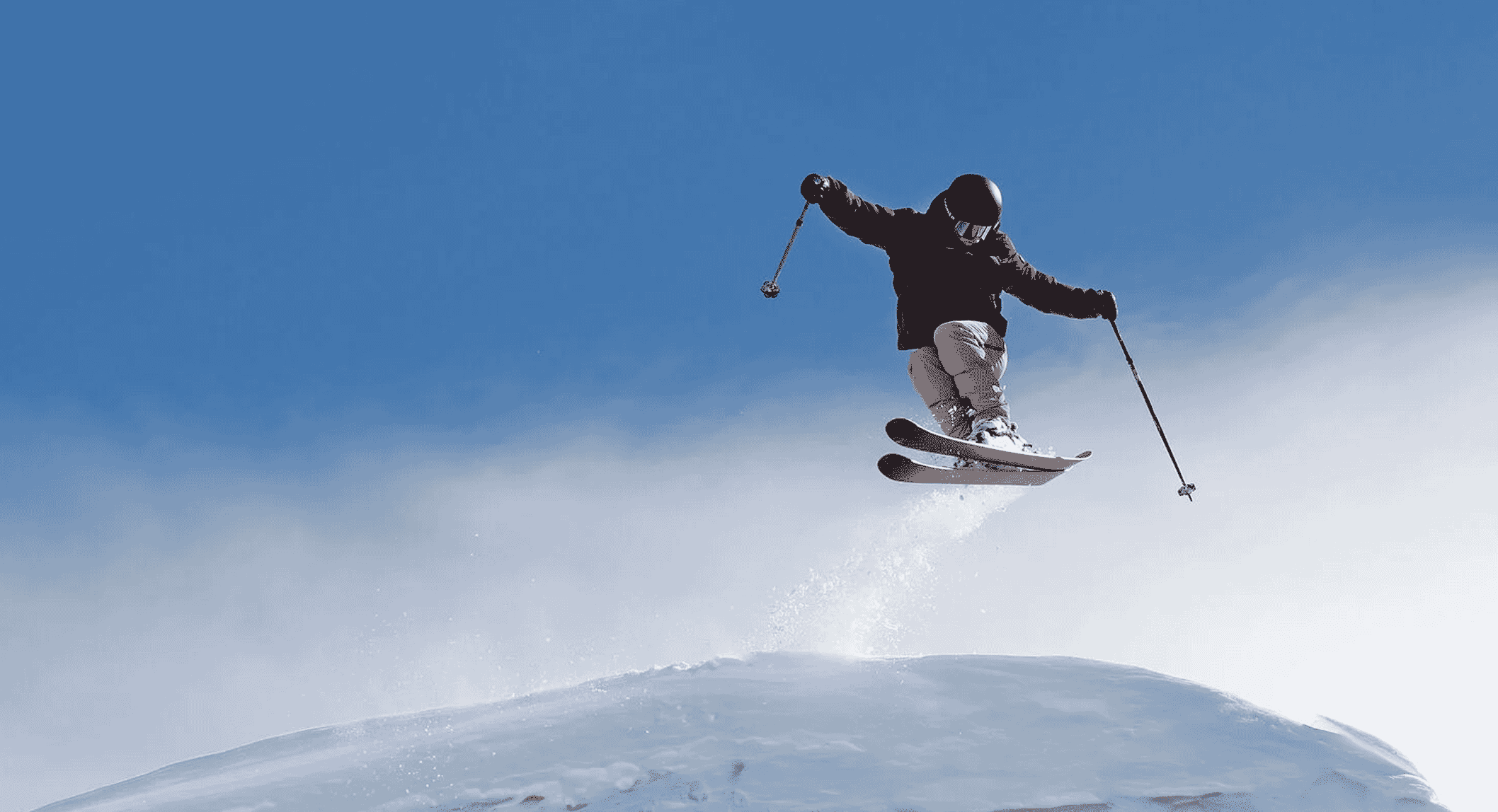 A skier in black jacket and light pants jumping against a clear blue sky.