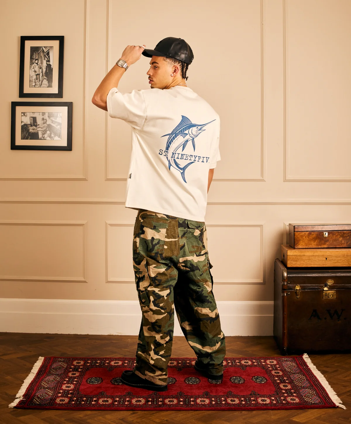 A model in a white t-shirt featuring a blue marlin graphic paired with camouflage cargo pants.