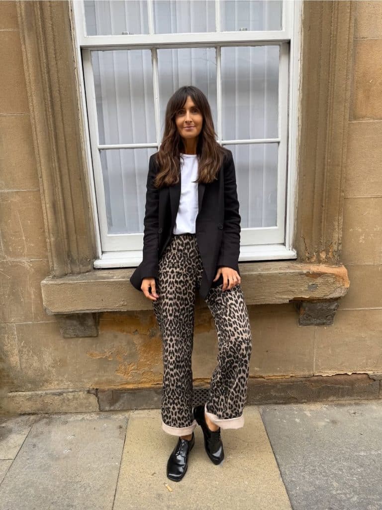 Woman in a black blazer and wide-leg leopard-print trousers.
