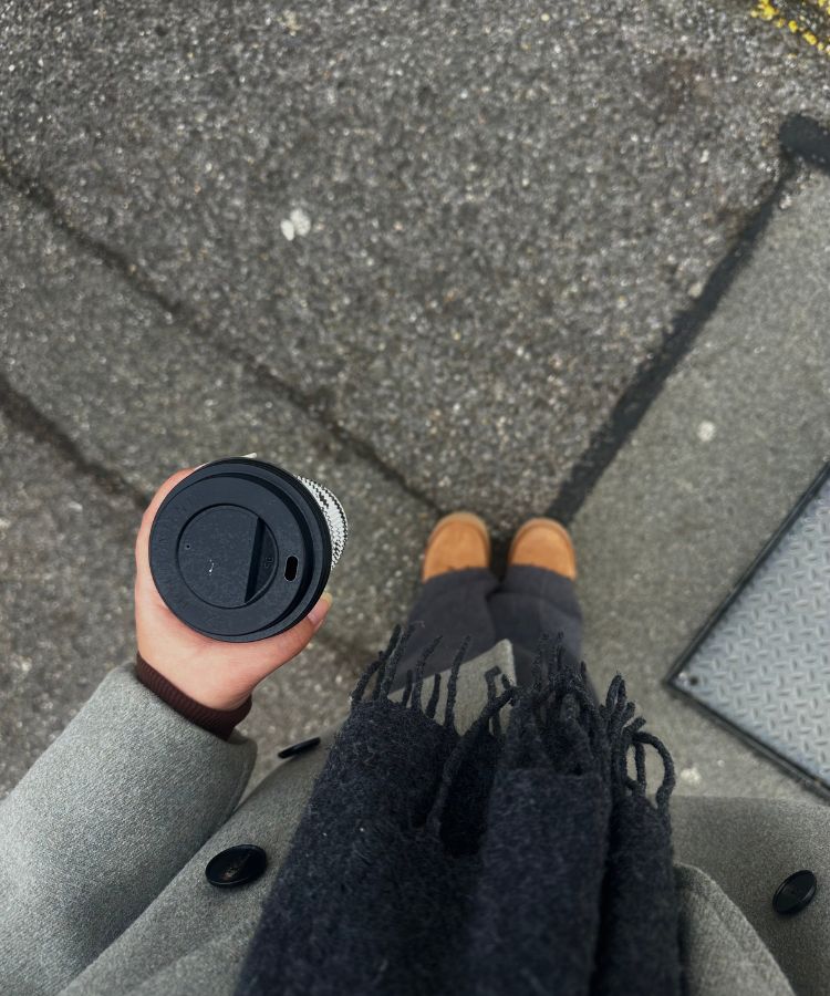 A person walking outdoors in winter attire holding a takeaway coffee cup.