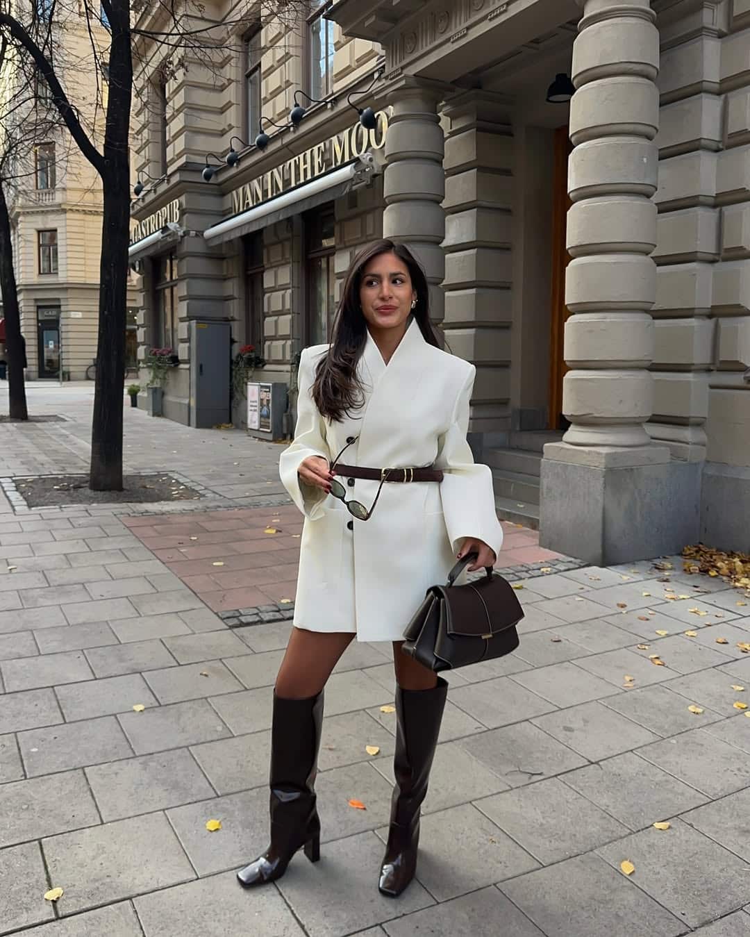 Full-body shot of a woman wearing a white blazer dress and brown glossy knee-high boots.