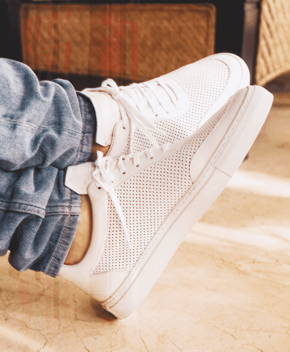 Close-up shot of white perforated sneakers worn with light-wash denim jeans.