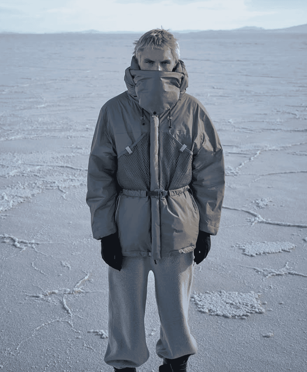 A person in a futuristic, oversized grey insulated parka on a vast salt flat.