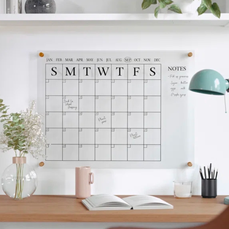 A clear acrylic wall calendar mounted on a white wall.