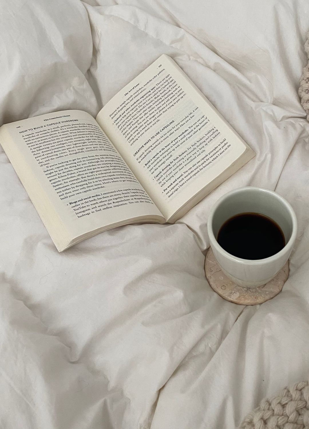 A person reading a book in a comfortable, dimly lit corner with a warm beverage nearby.