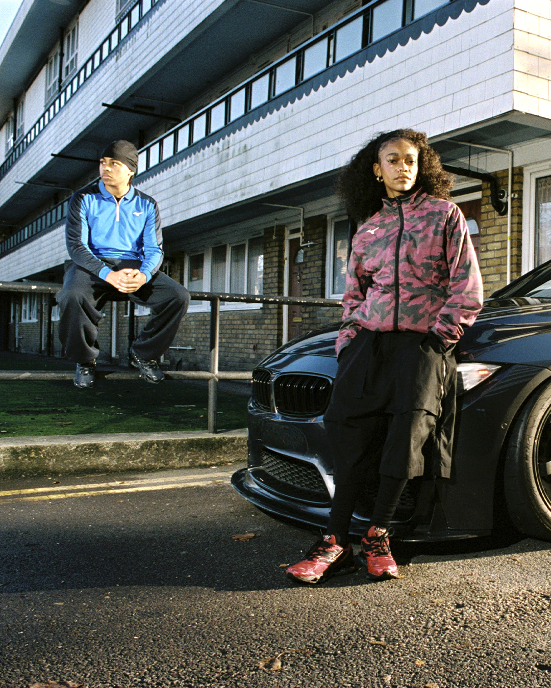 A woman in a pink camouflage jacket and cargo pants leaning against a car to showcase street style.