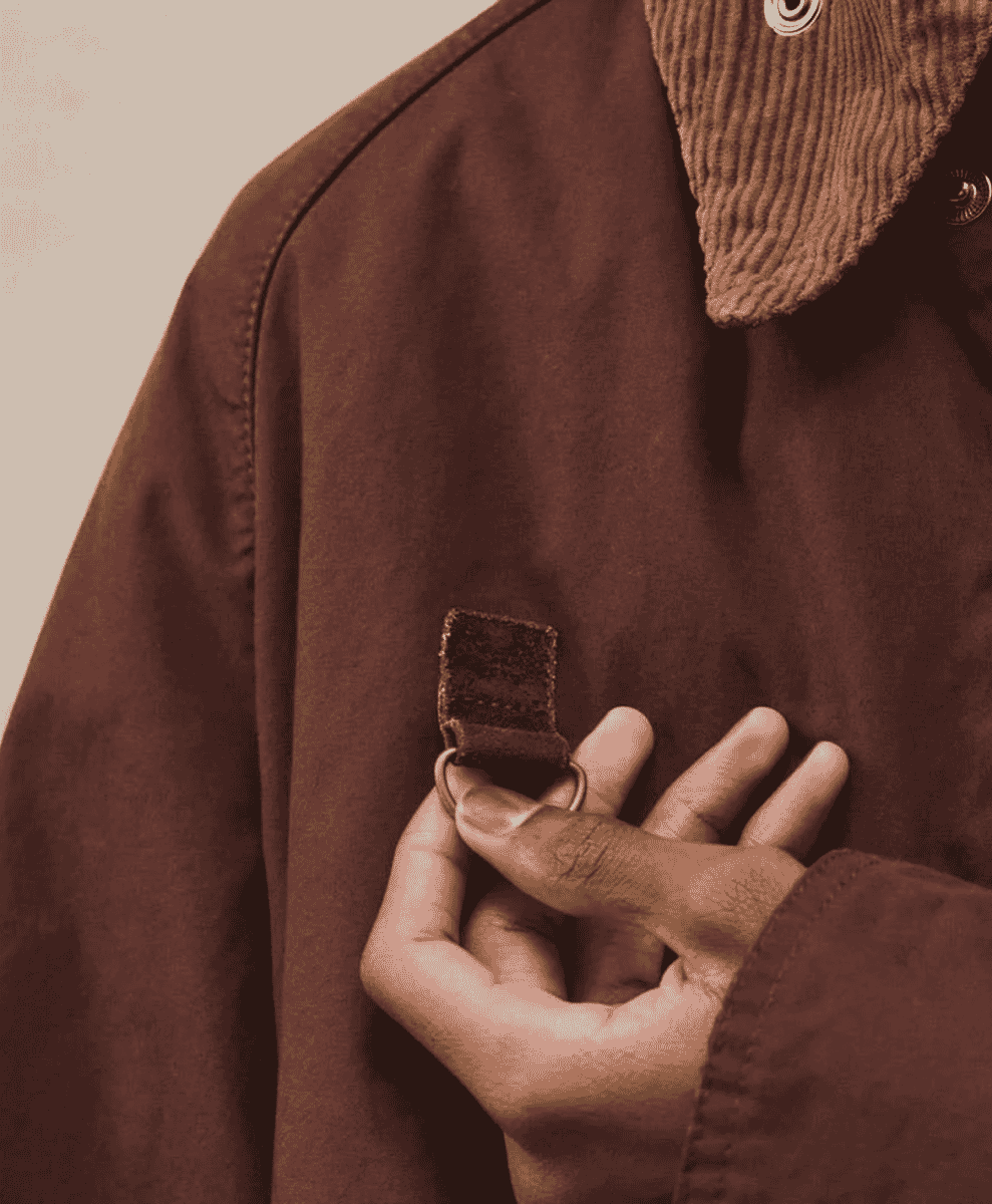 Sepia-toned close-up of a corduroy collar and leather strap detail on a waxed cotton jacket.