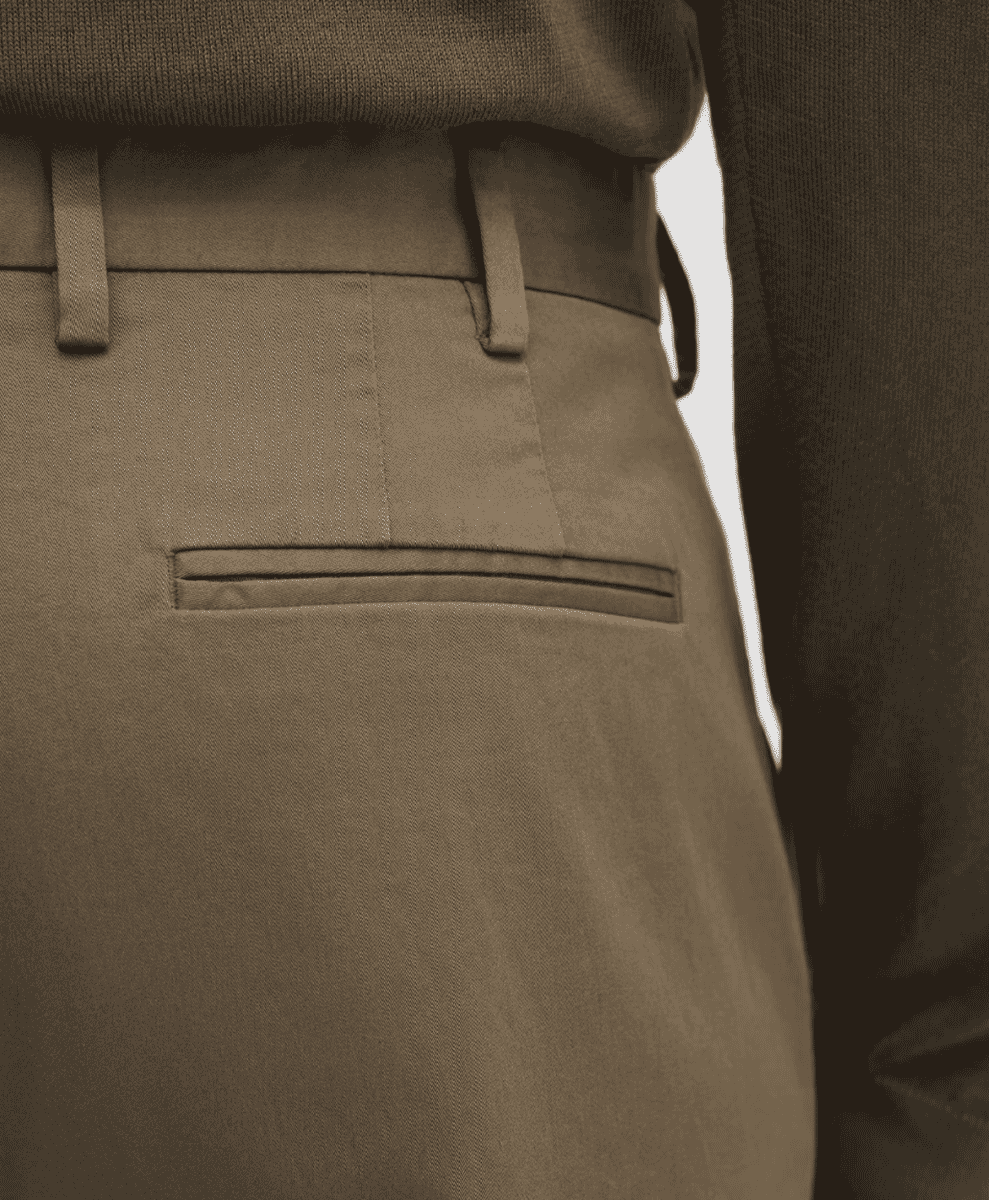 Close-up of beige chinos featuring a welt pocket and clean waist tailoring.
