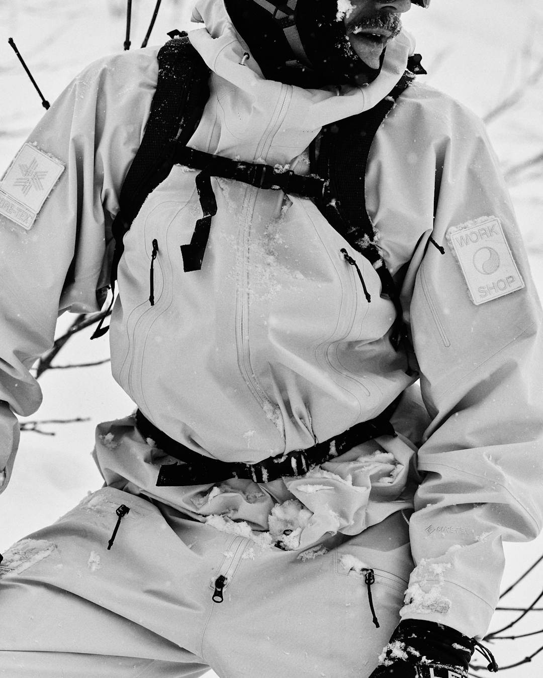 A man in a light-colored GORE-TEX technical jacket standing in a snowy outdoor setting.