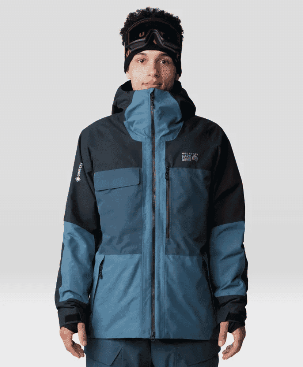 A model in a blue and black Mountain Hardwear Gore-Tex jacket with hood and goggles.
