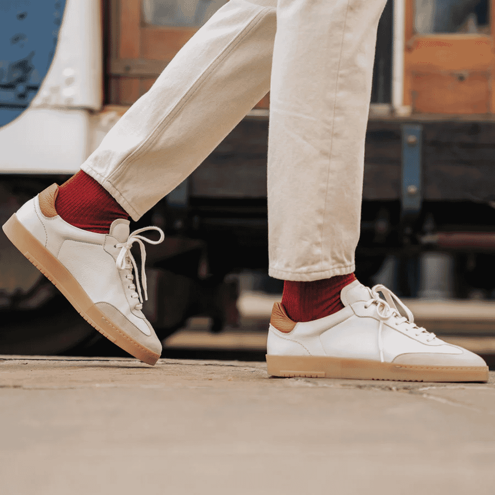 Man in cream-colored trousers and red socks wearing white leather sneakers with gum soles.