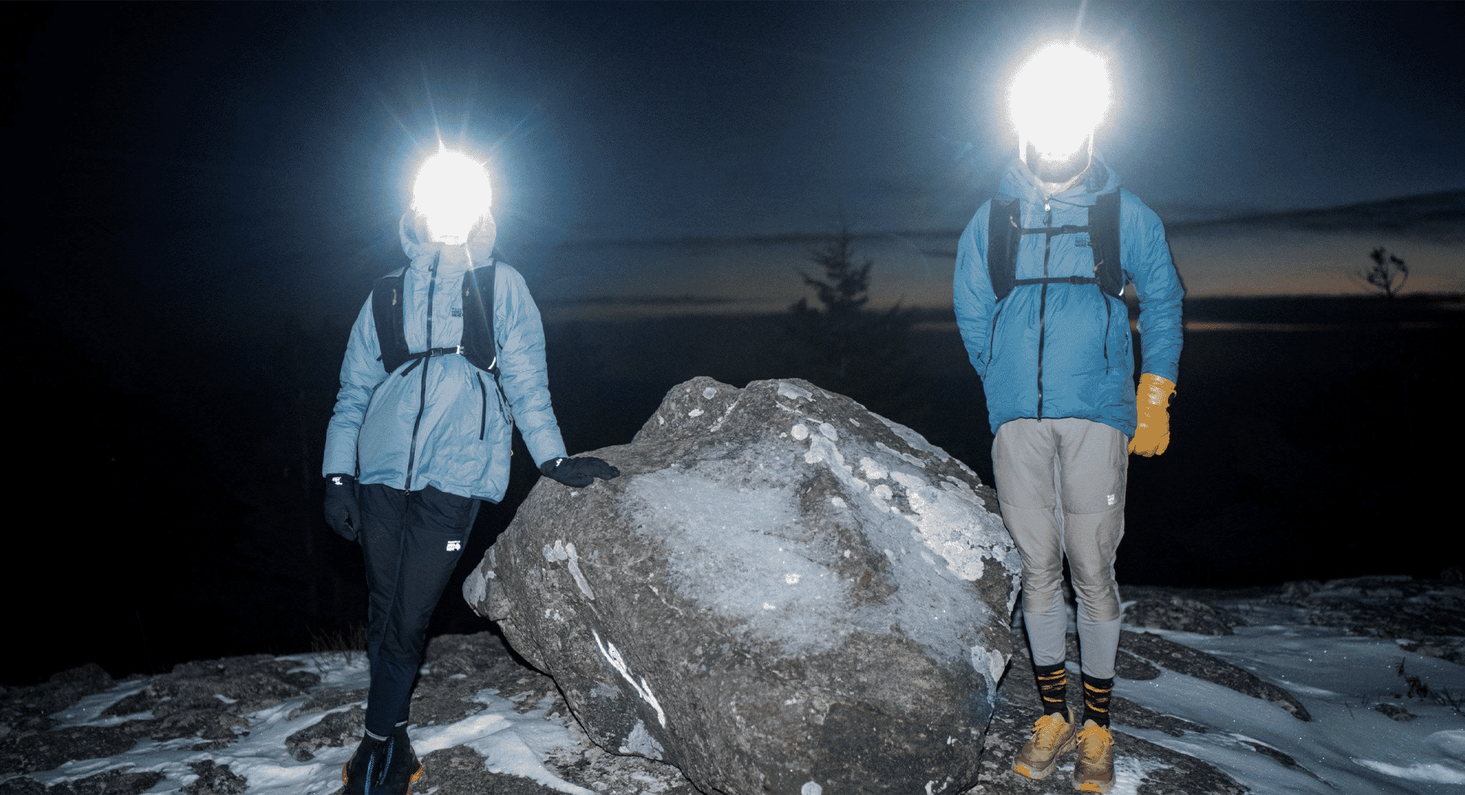 Hikers in winter gear under headlamp illumination on a snowy mountain at night.