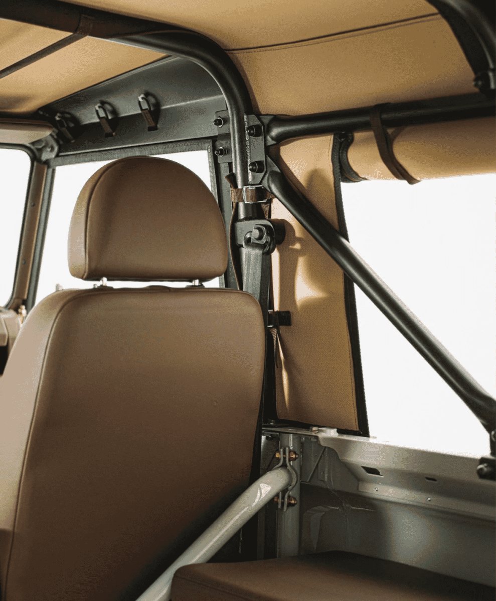 Interior view of a Defender 90 highlighting the black roll cage and beige fabric roof lining.