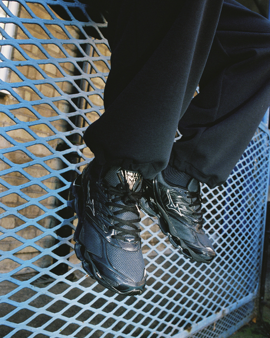 Close-up of glossy dark blue Mizuno shoes highlighting the mechanical wave sole on a blue metal grate.