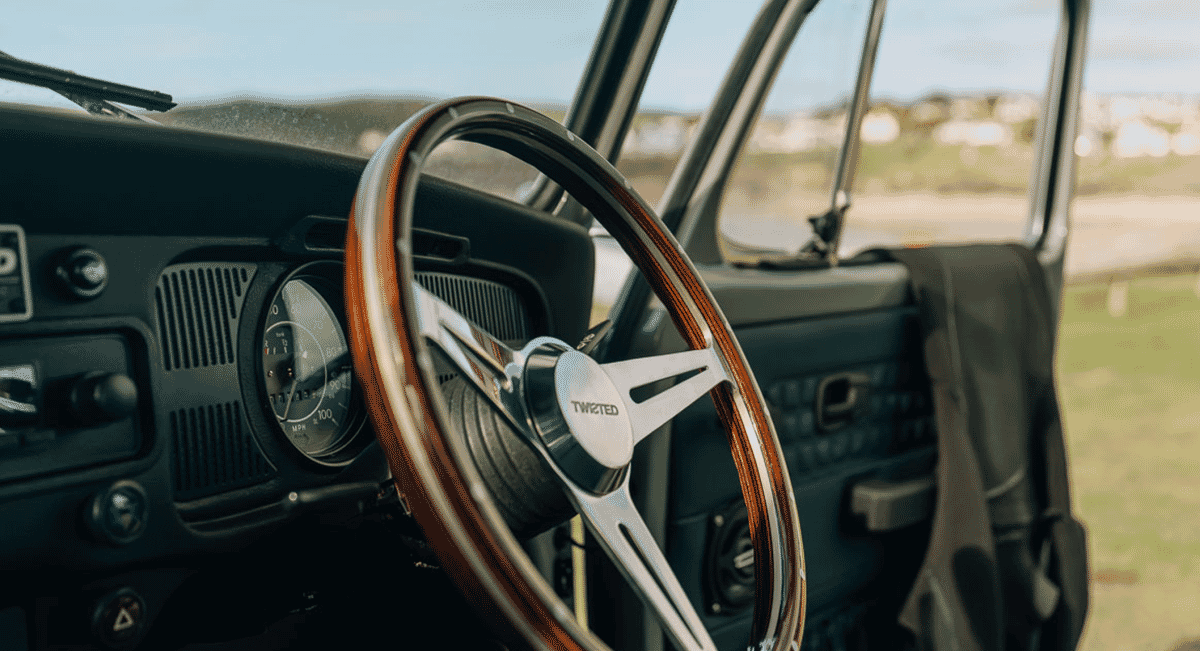 Interior shot of a vintage vehicle showing a wooden steering wheel, leather dashboard, and analog gauges.