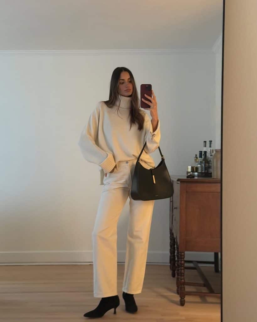 A mirror selfie of a woman wearing an oversized cream turtleneck, matching wide-leg trousers, and black ankle boots.