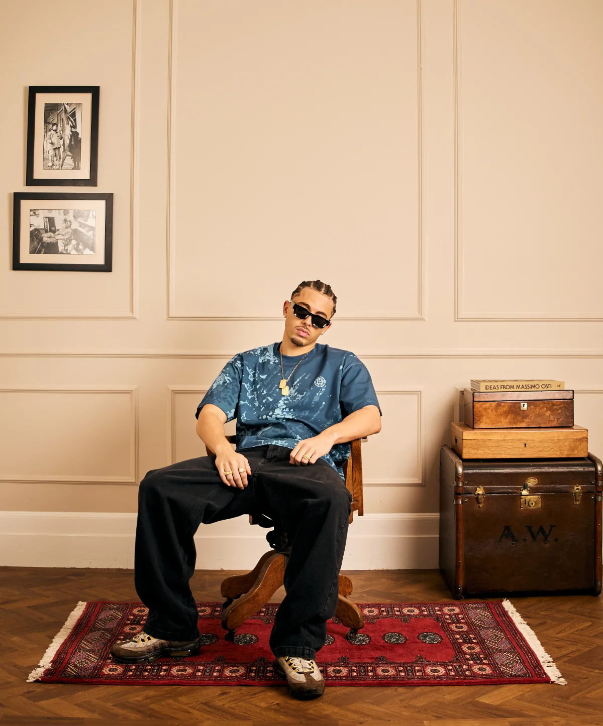 Model sitting in a wooden chair wearing a blue tie-dye t-shirt and wide-leg dark jeans.