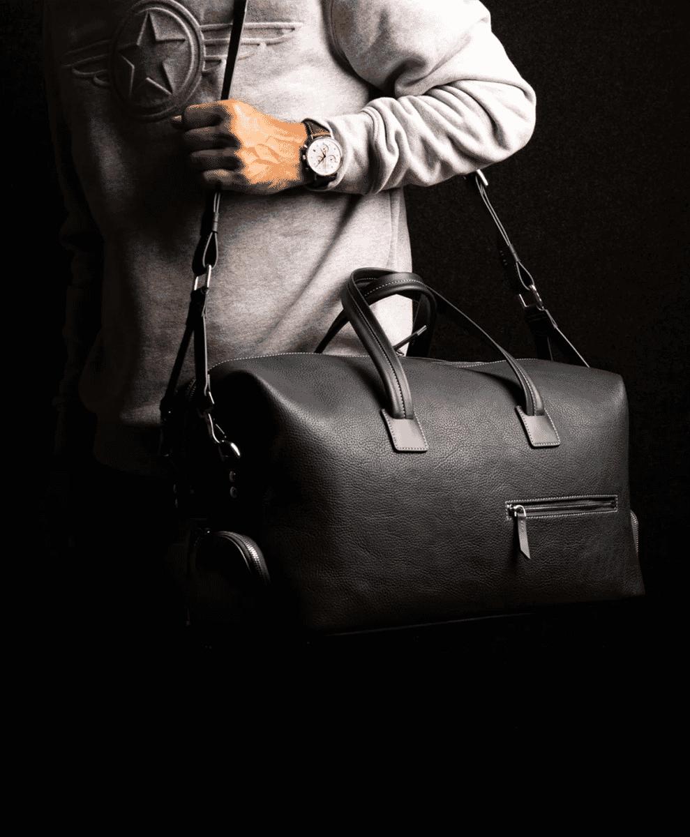 A man carrying a black leather duffel bag, emphasizing a sophisticated travel look.