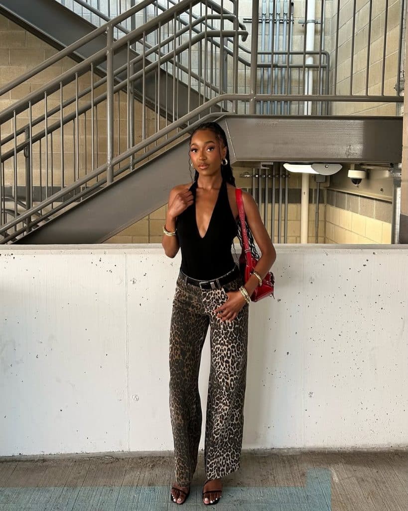 Woman in a black halter top, leopard pants, and a red shoulder bag.