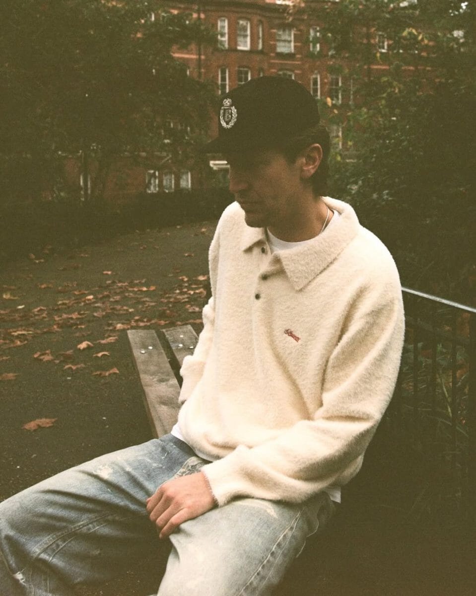 Man wearing a cream fuzzy polo sweater on a park bench.