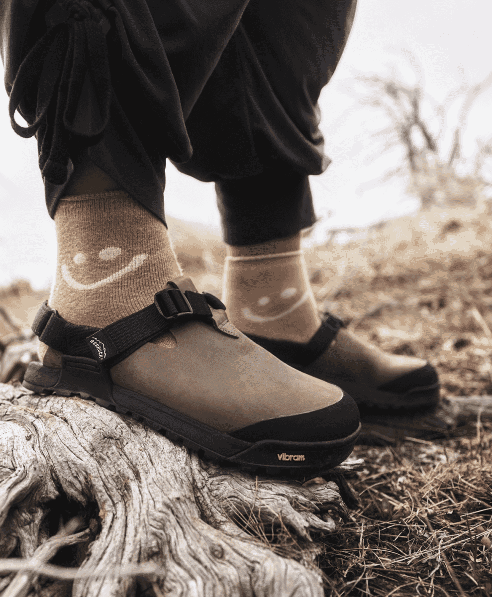 Close-up of brown suede clogs worn with yellow smiley-face socks.