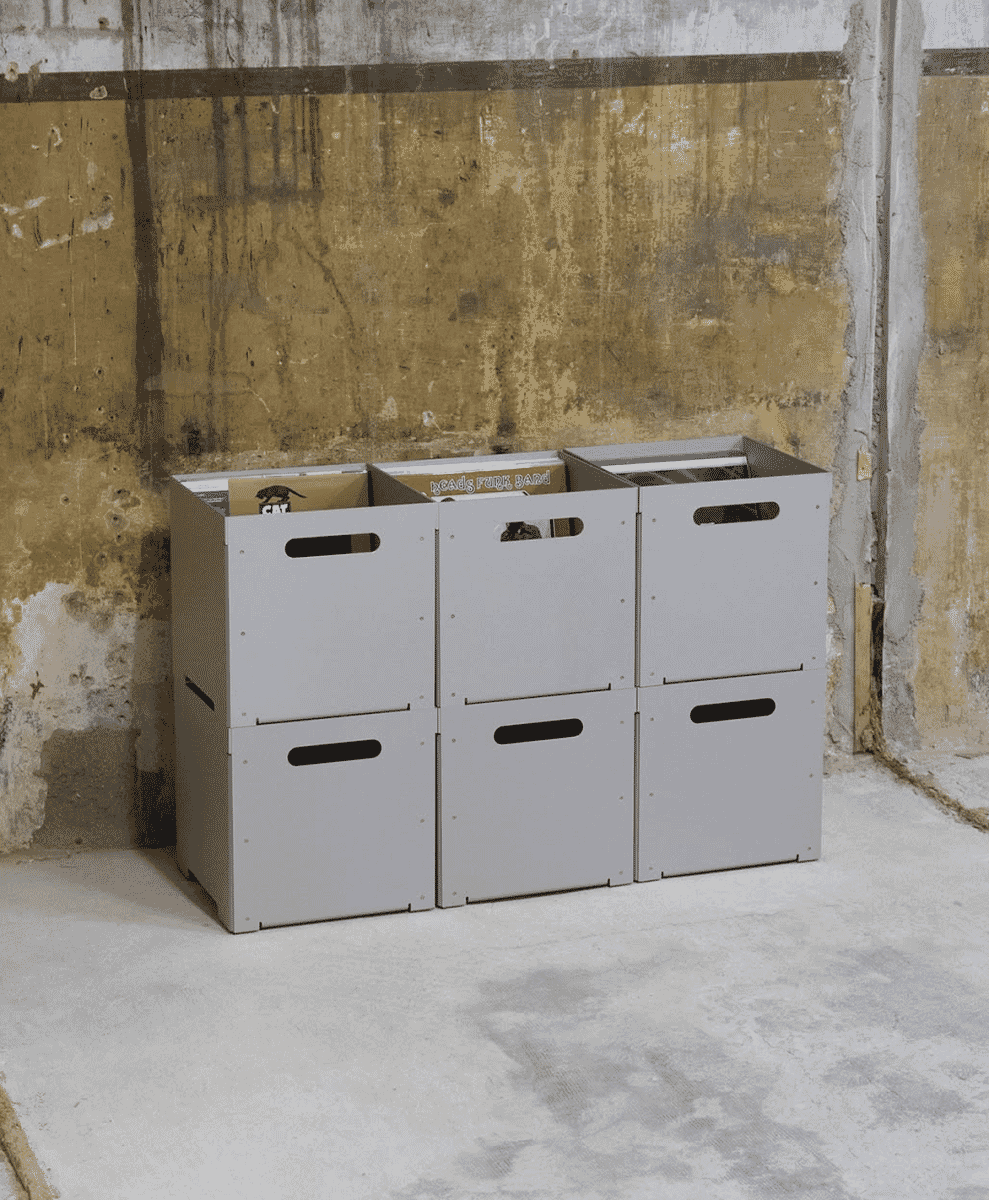 Three gray modular storage bins containing vinyl records against a concrete wall.