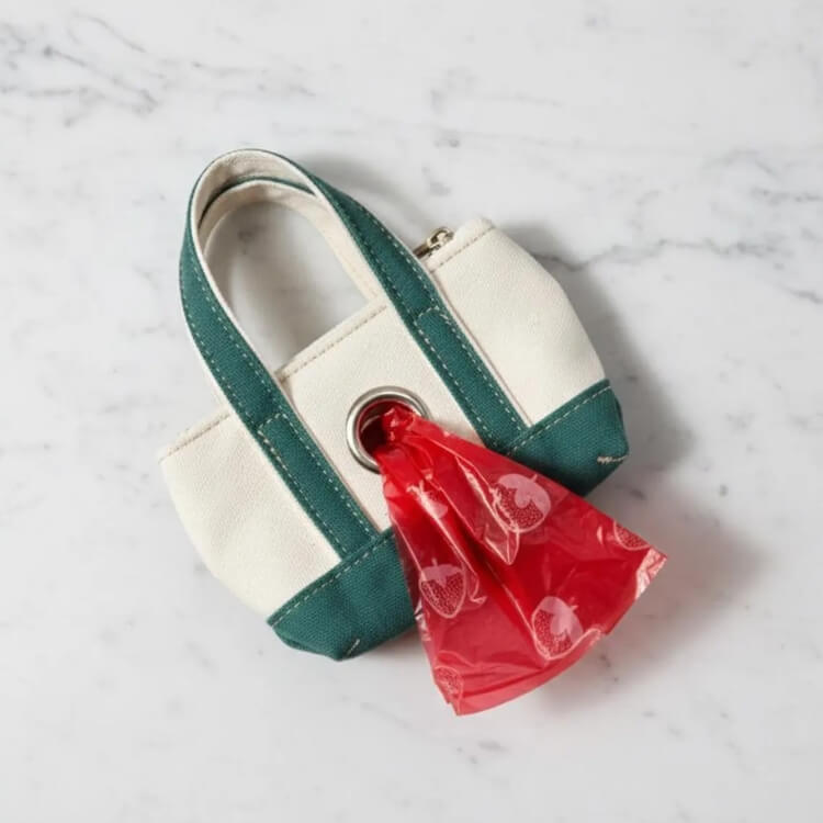A miniature tote bag designed to hold dog poop bags, attached to a larger handbag.