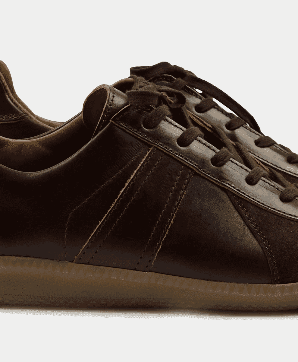 Close-up of a dark brown leather and suede military-style trainer with visible stitching.