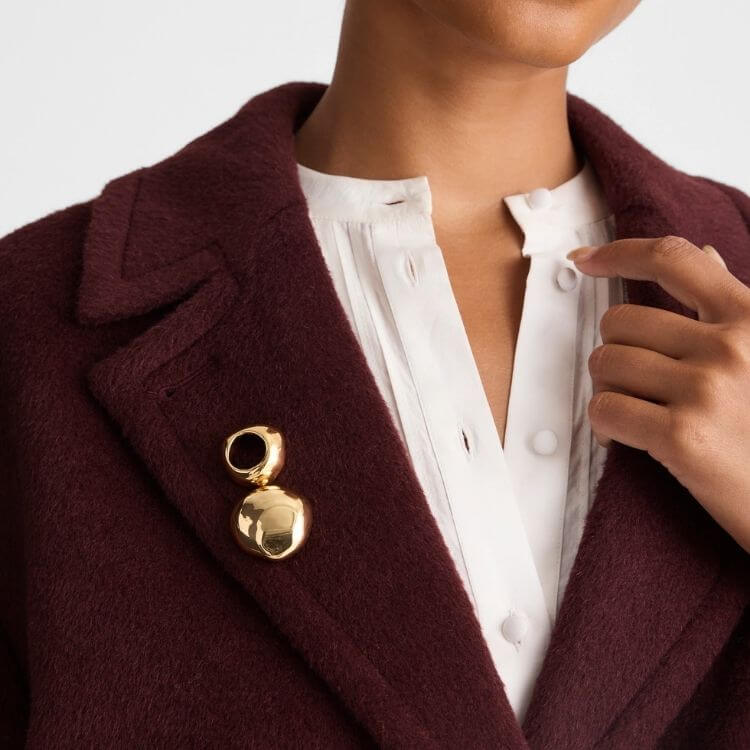 A contemporary gold-tone brooch with a sculpted cutout design.