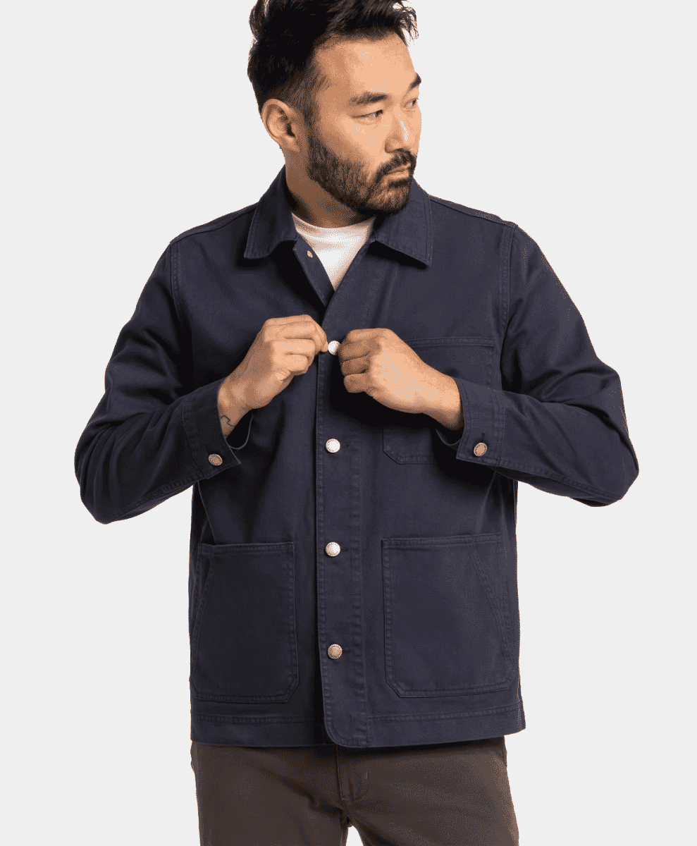 Close-up of a man buttoning a navy work jacket with flap pockets.
