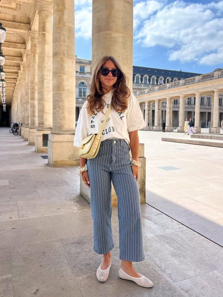 Full body shot of a woman in striped wide-leg pants, a graphic tee, and black ballet flats.