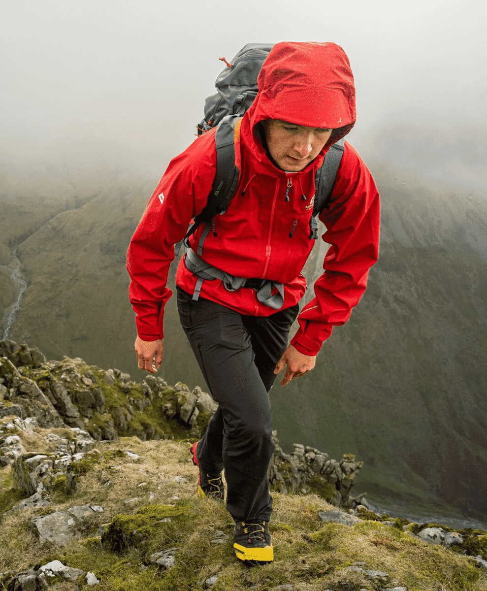 A hiker in a red waterproof shell jacket on a foggy mountain ridge.