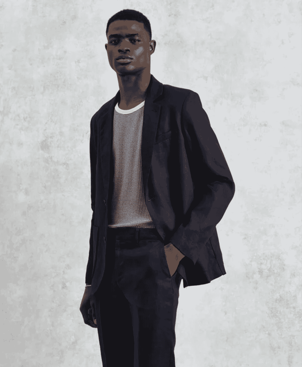 A man wearing a dark textured blazer over a ribbed knit sweater against a neutral studio background.