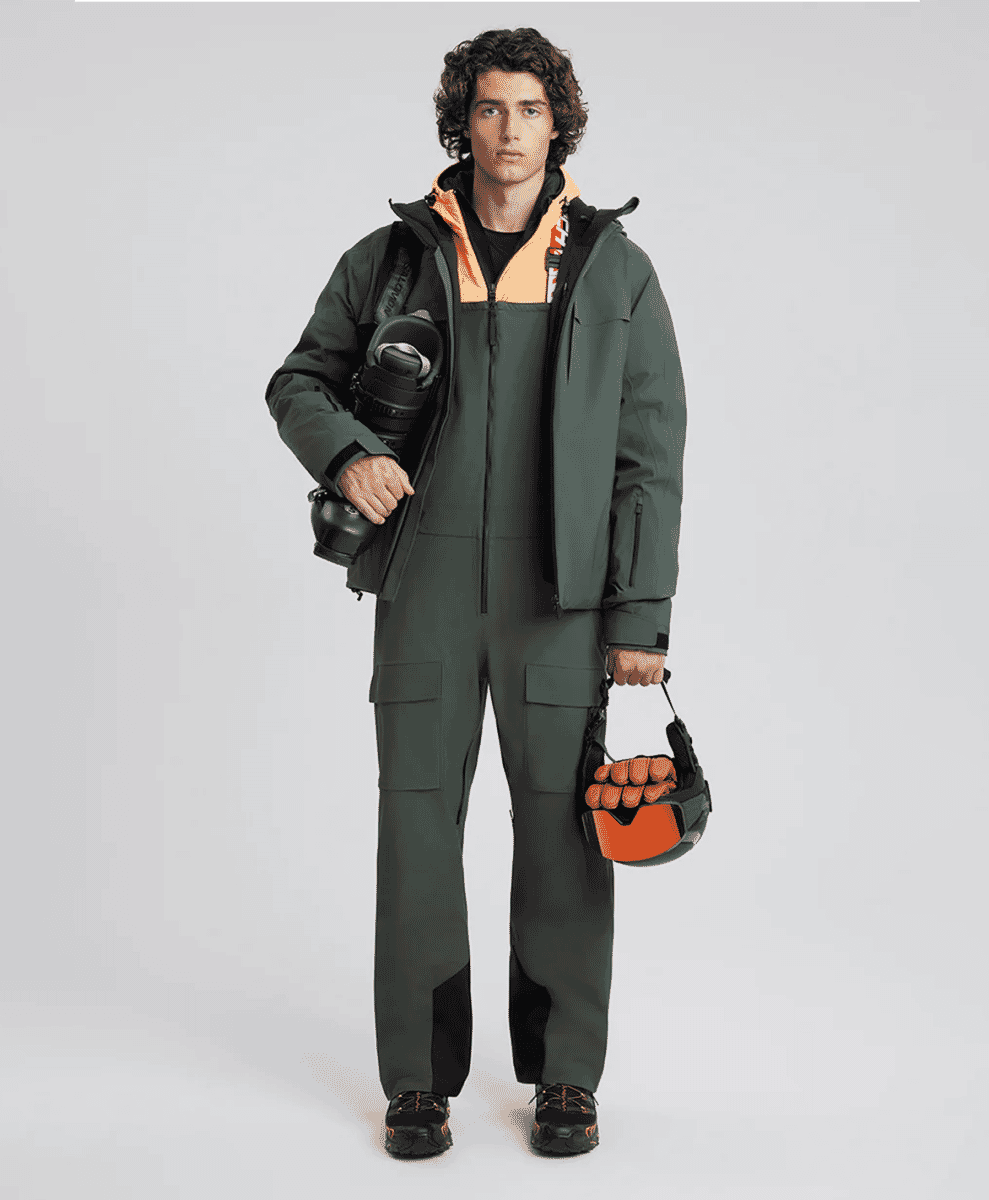 A model in a dark teal ski-style jumpsuit with orange accents.