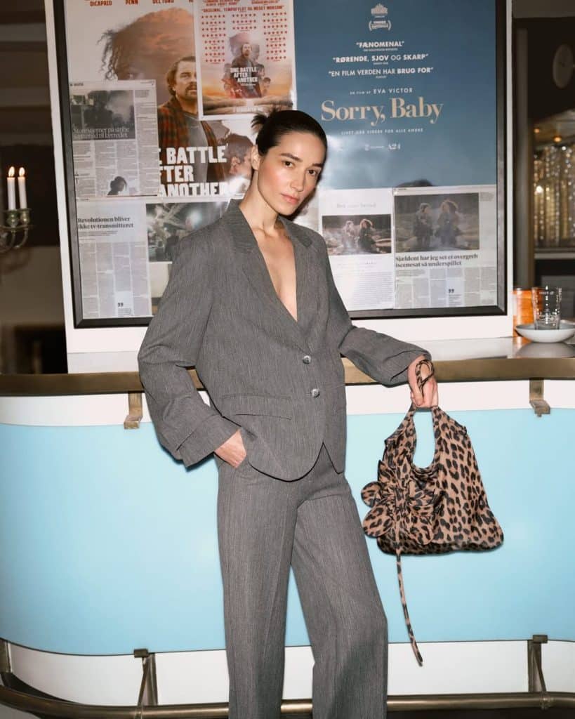 A woman posing confidently in a pinstripe suit against a backdrop of posters.