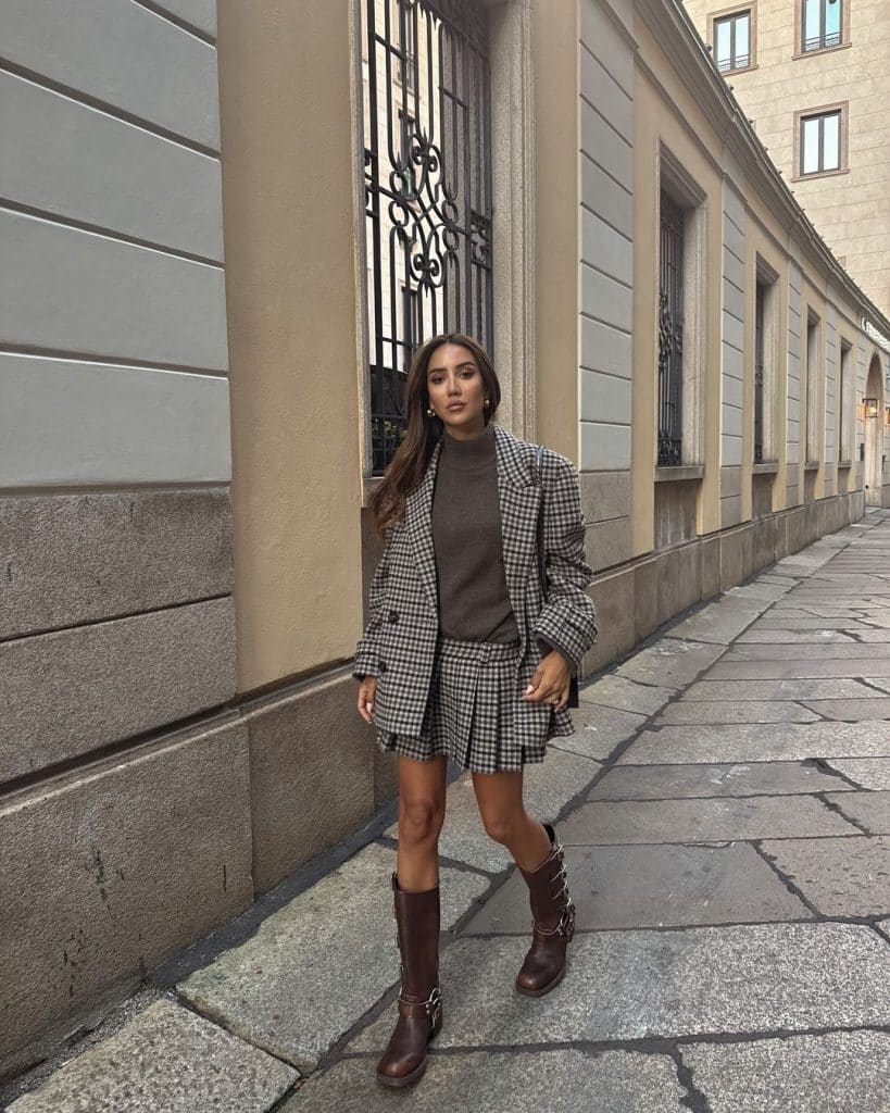 Woman in a plaid blazer and pleated skirt set with brown knee-high boots.