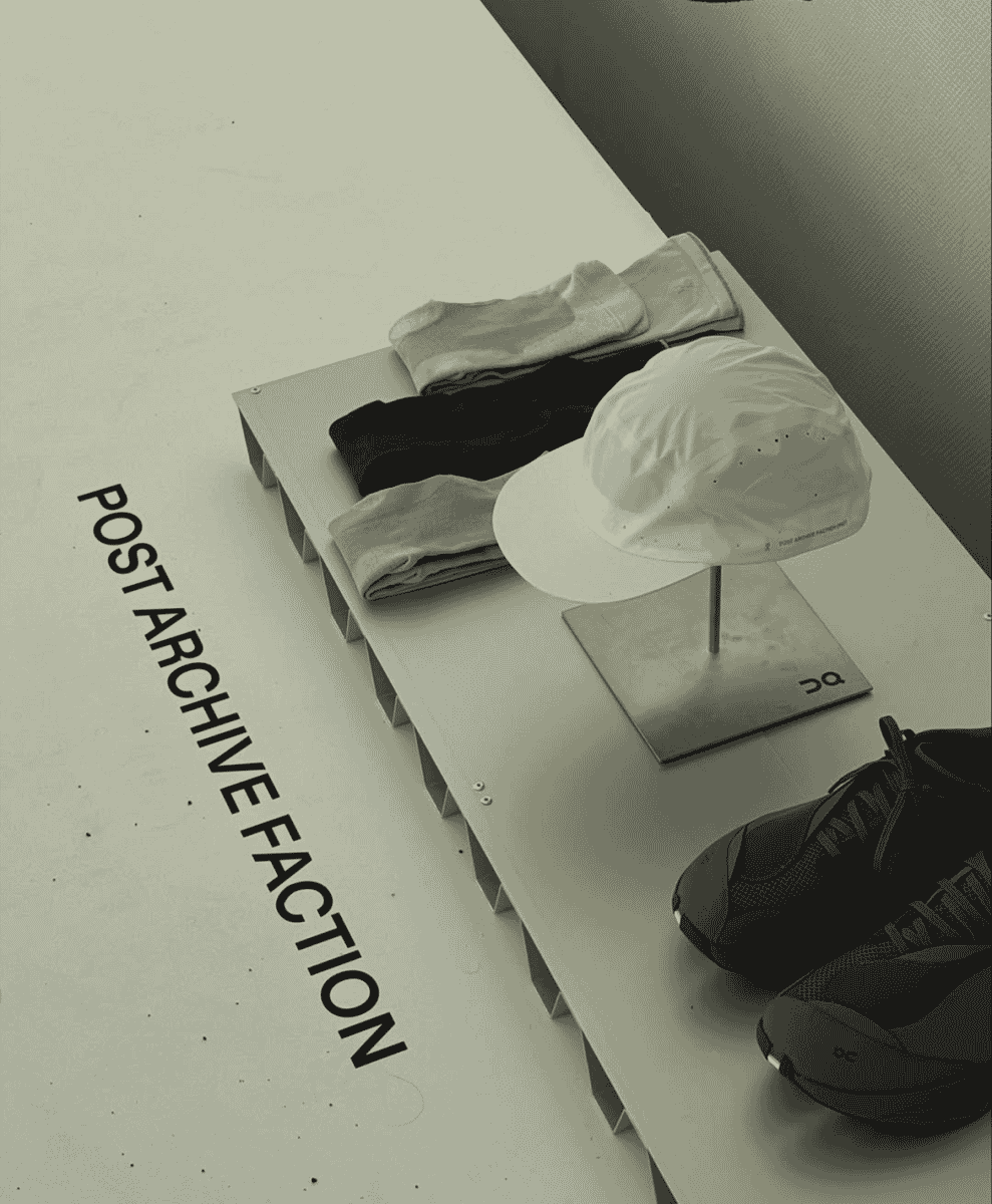 Minimalist shelf display featuring folded athletic socks, a white cap, and running sneakers with PAF branding.