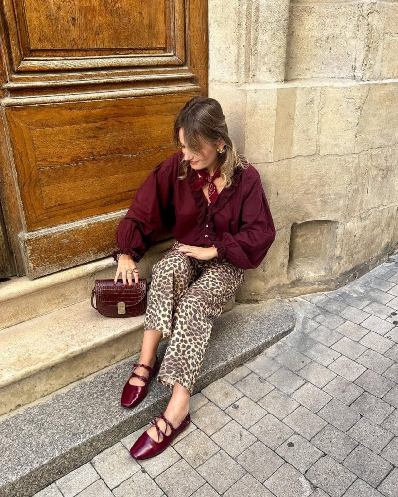 Woman in a burgundy ruffled blouse and leopard-print pants holding a croc-texture handbag.