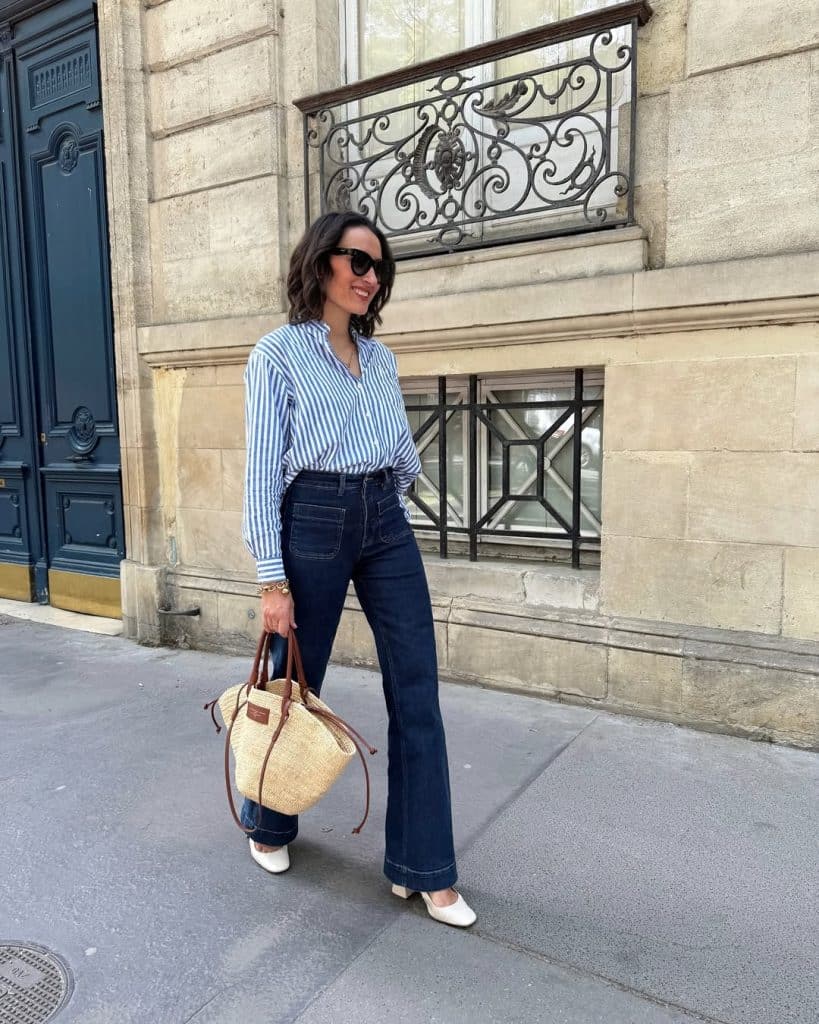 A woman wearing a blue and white striped button-down shirt tucked into dark wide-leg jeans.