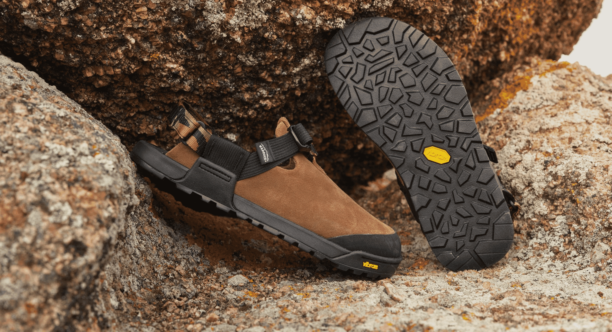 Brown suede hiking sandals with black straps shown on sharp rocky ground.