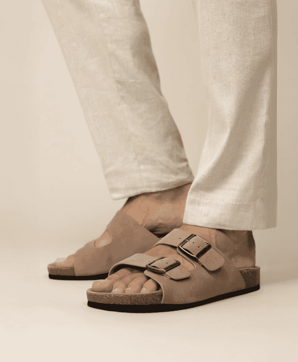 Beige suede double-strap sandals paired with light linen trousers.