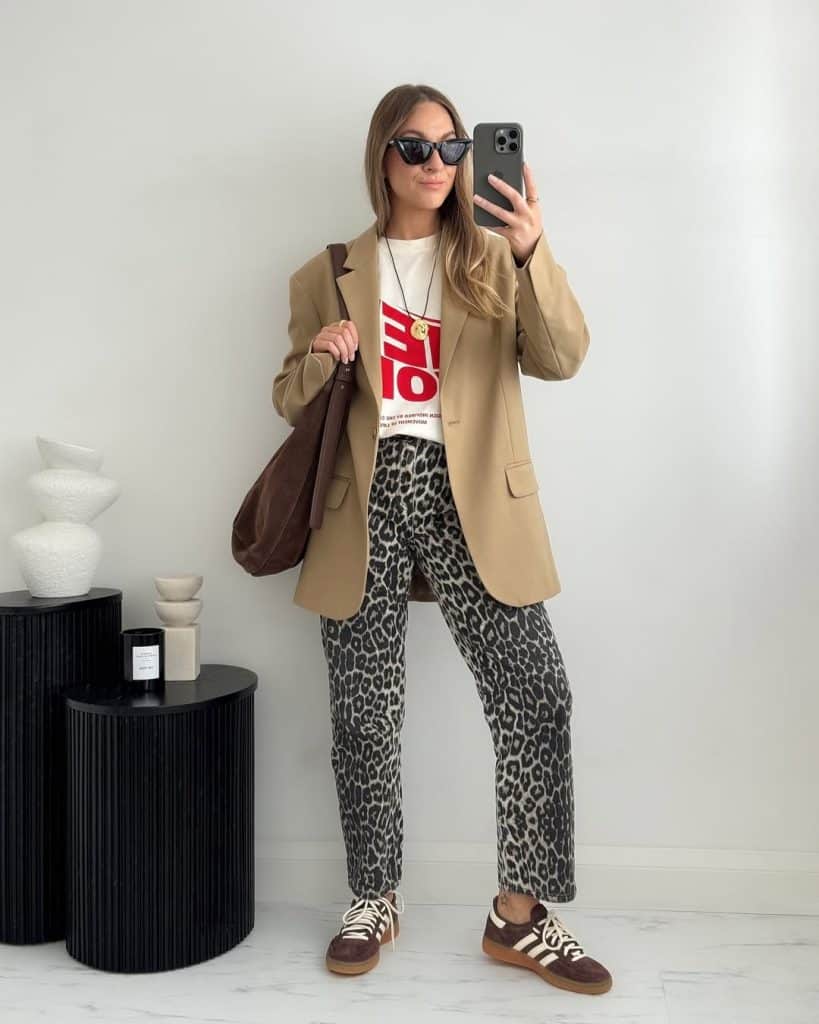 Mirror selfie of a woman in a camel blazer, graphic tee, and leopard pants.